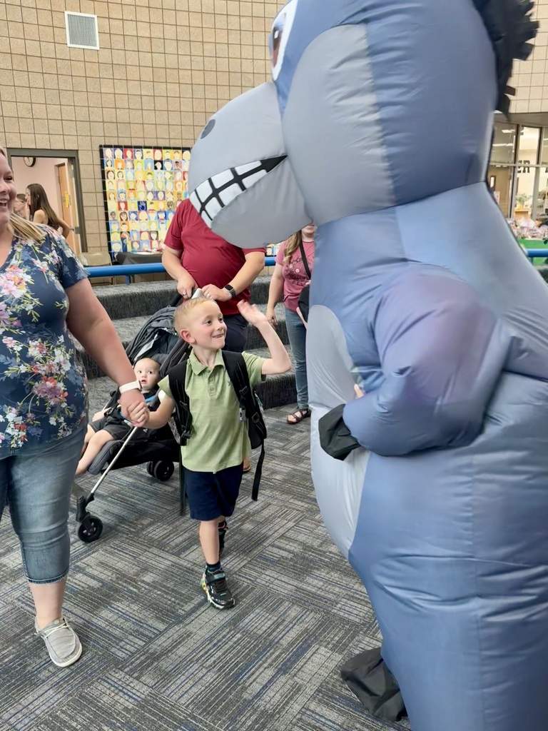 student giving Miss G (wearing a donkey costume) a high five, parents and other students are seen smiling in the background
