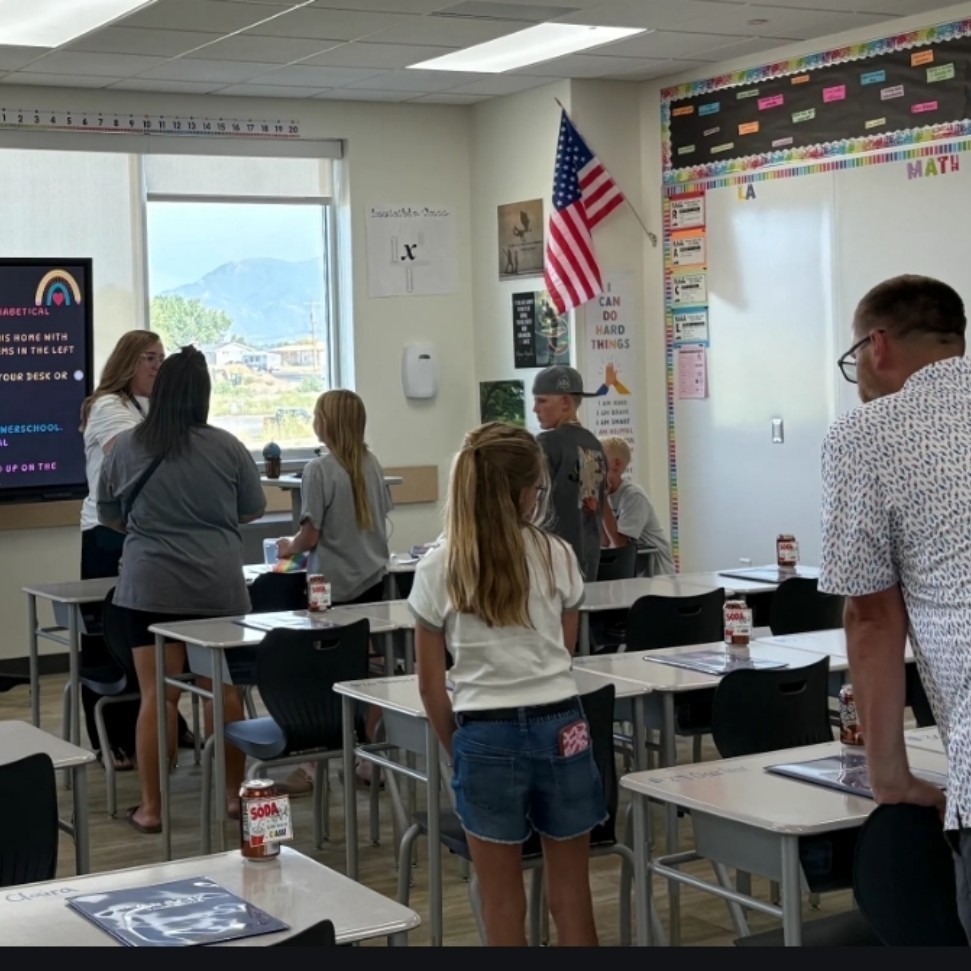 Mrs. Smith's classroom full of students and parents standing near desks. A digital display reads:
"WELCOME!"
"Take a minute to find your seat. They are in alphabetical order starting in the front, south corner."
"There is a folder on your desk. You will take this home with you tonight."
"If you brought supplies, you can place them in your desk or on the back table."
"Make sure you have downloaded the WSD app."
Email reminders and first-day instructions follow.