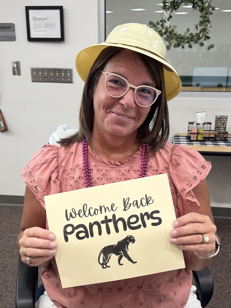 The school librarian holding a "welcome back panthers" sign and wearing a safari hat
