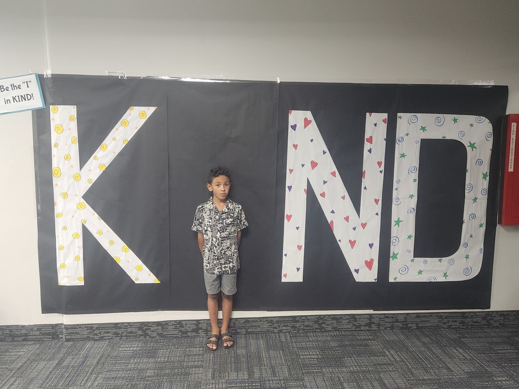 Students in front of black sign with bold papered letters spelling out the work KIND with students posing as the 'i' 