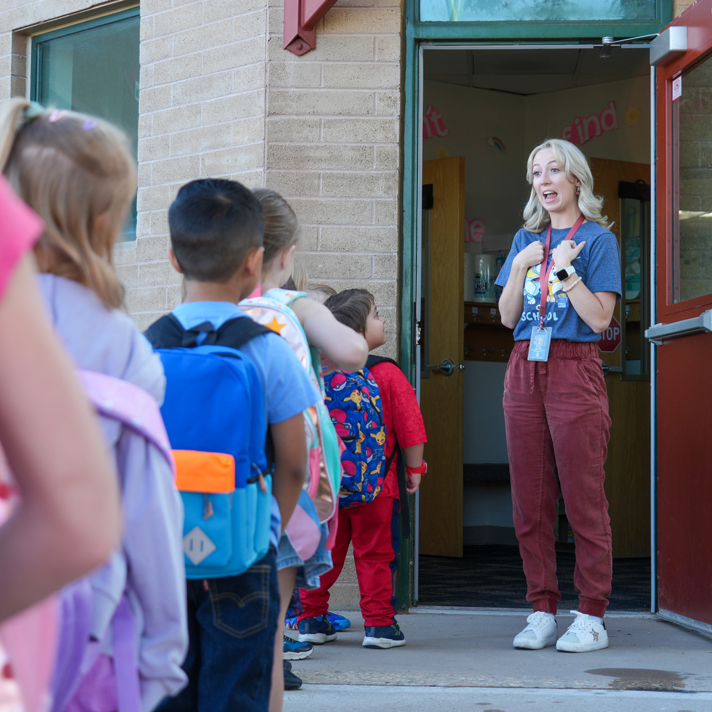 A teacher greets the students at the door of her classroom