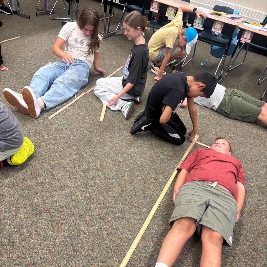 students measuring each other's height in a classroom