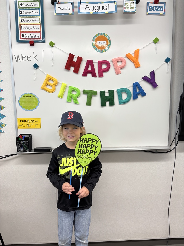 Student standing with a birthday balloon sign that says happy happy happy birthday in front of a happy birthday banner. 