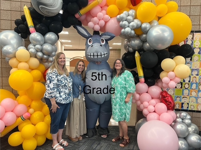5th grade teachers standing under a balloon arch and next to Miss G in a donkey costume. 5th grade is written on the picture in text. 