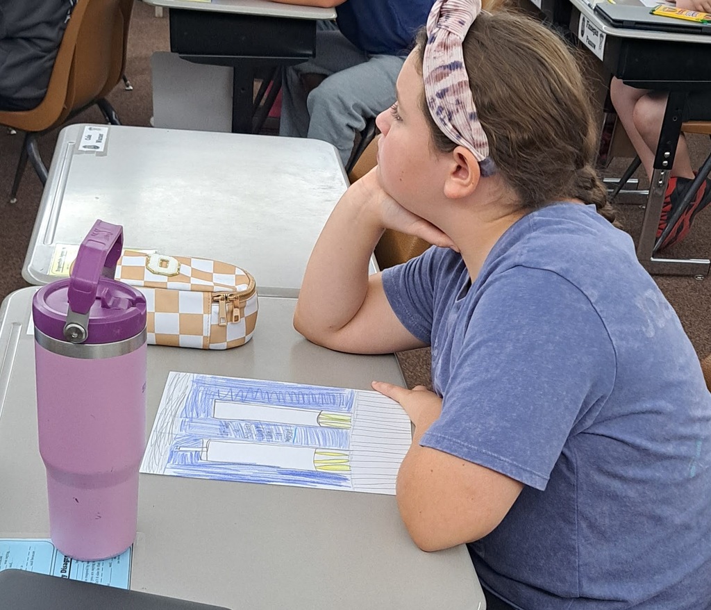 Female student sits at her desk in front of a drawing of the twin towers she made.