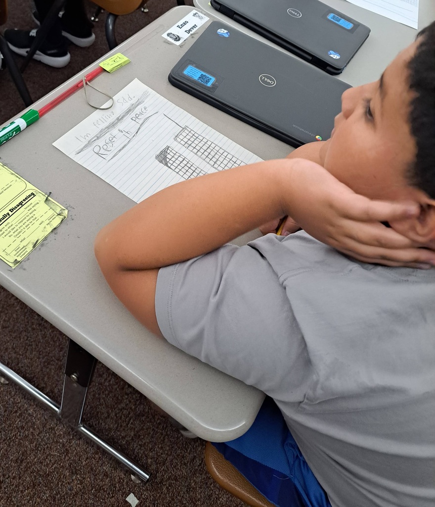 Male student sits at his desk in front of a drawing he has made that says rest in peace.