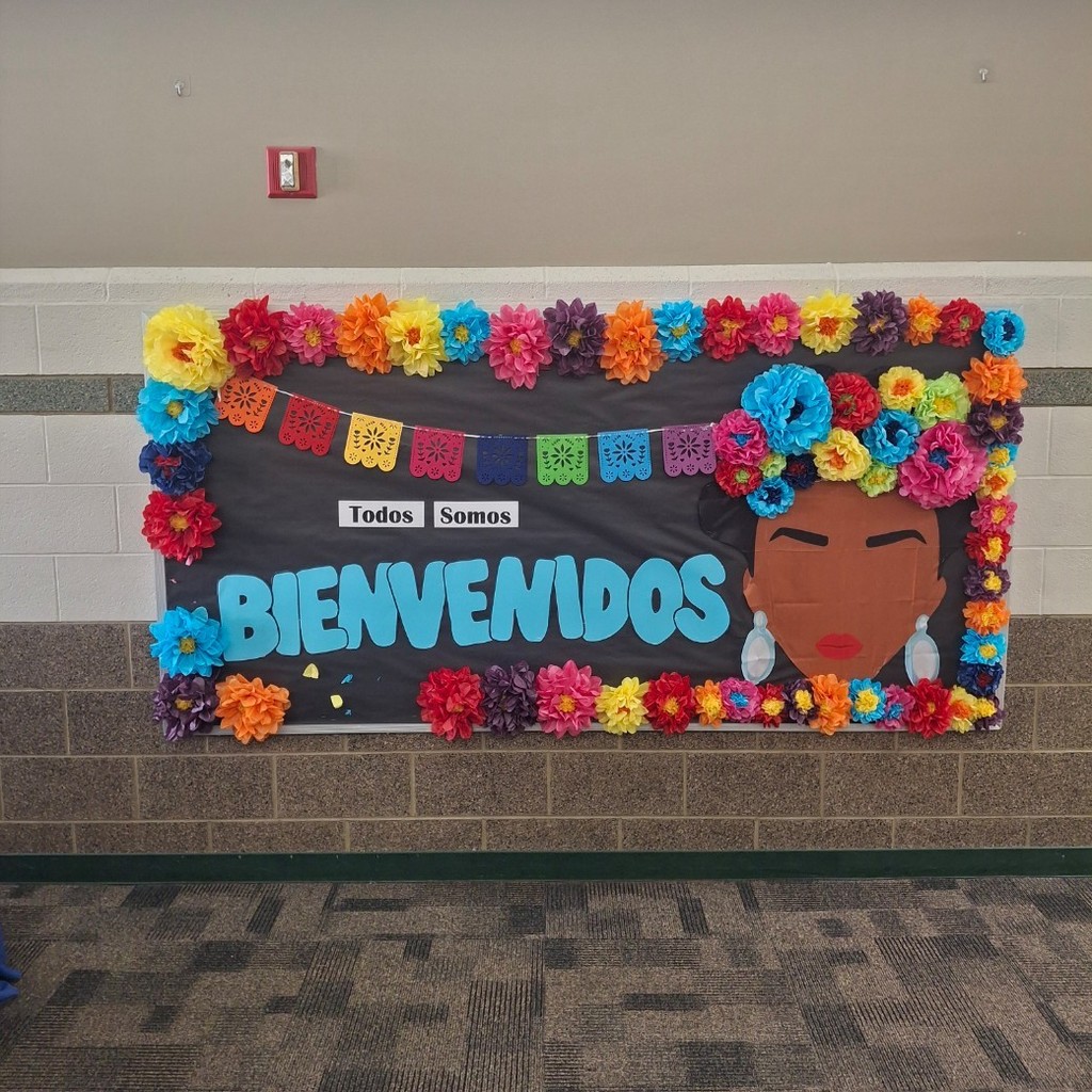 A bulletin board with colorful flags and flowers. Todos solos Bienvenidos