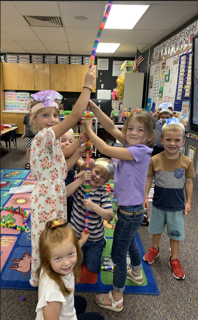A group of elementary school children are having fun in a classroom, building a tall, colorful tower together.