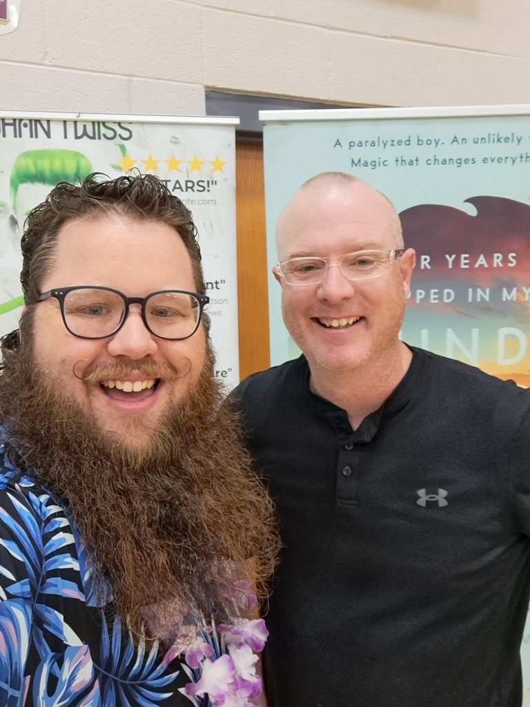 Two males smiling for a selfie; one with a long beard and glasses, and the other with short hair and glasses.