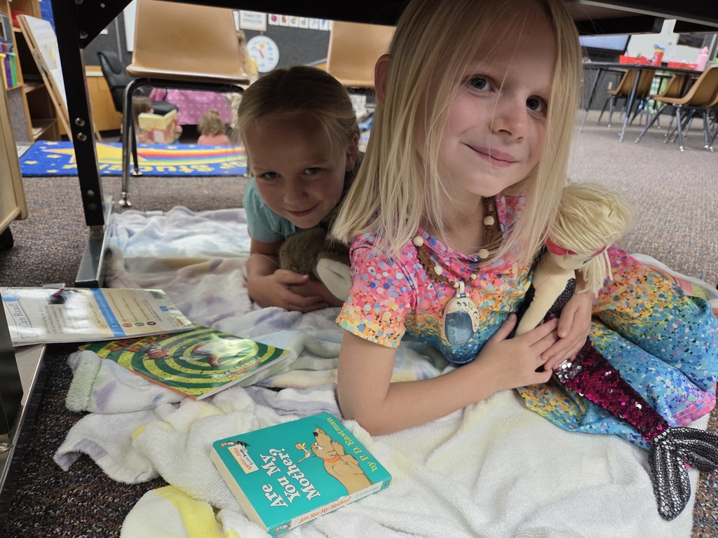 Students with books and blankets under a table. 