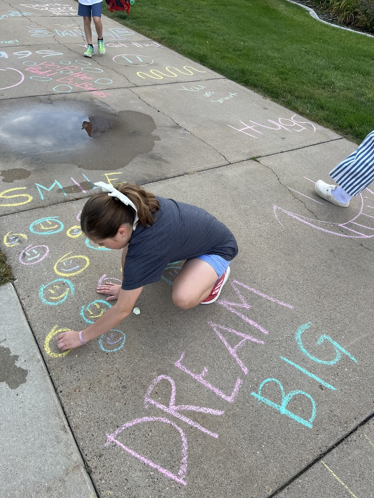 Student writing positive messages and art with sidewalk chalk