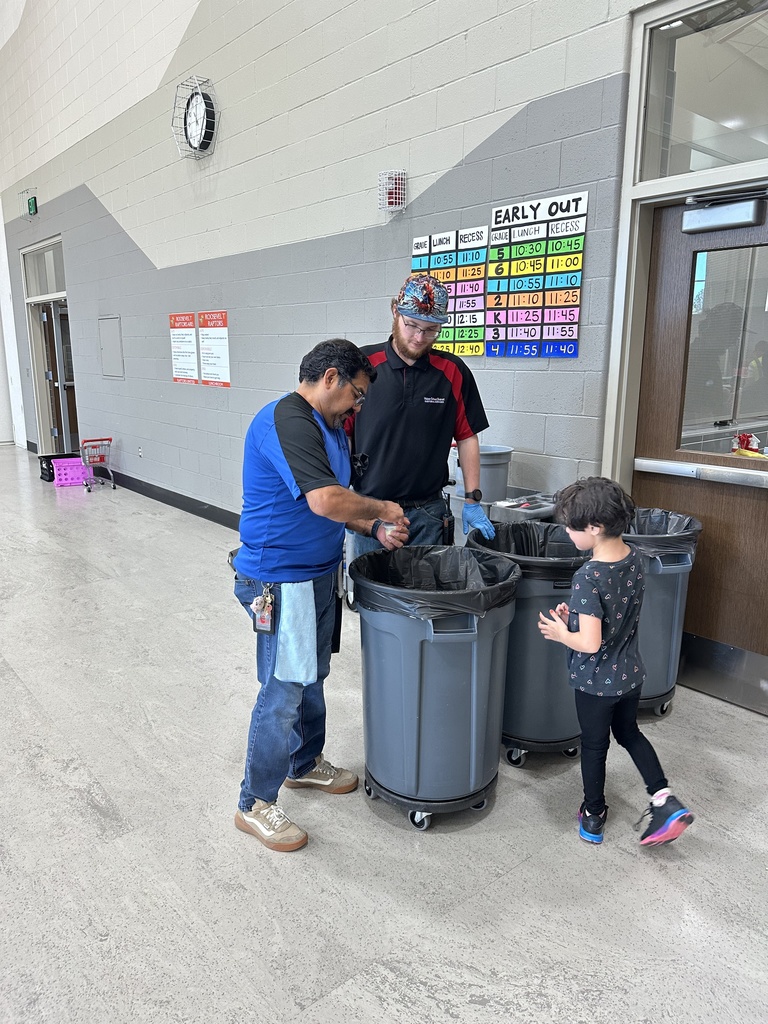 two custodians helping a student who is needs help with her lunch. All people are standing around two trash cans