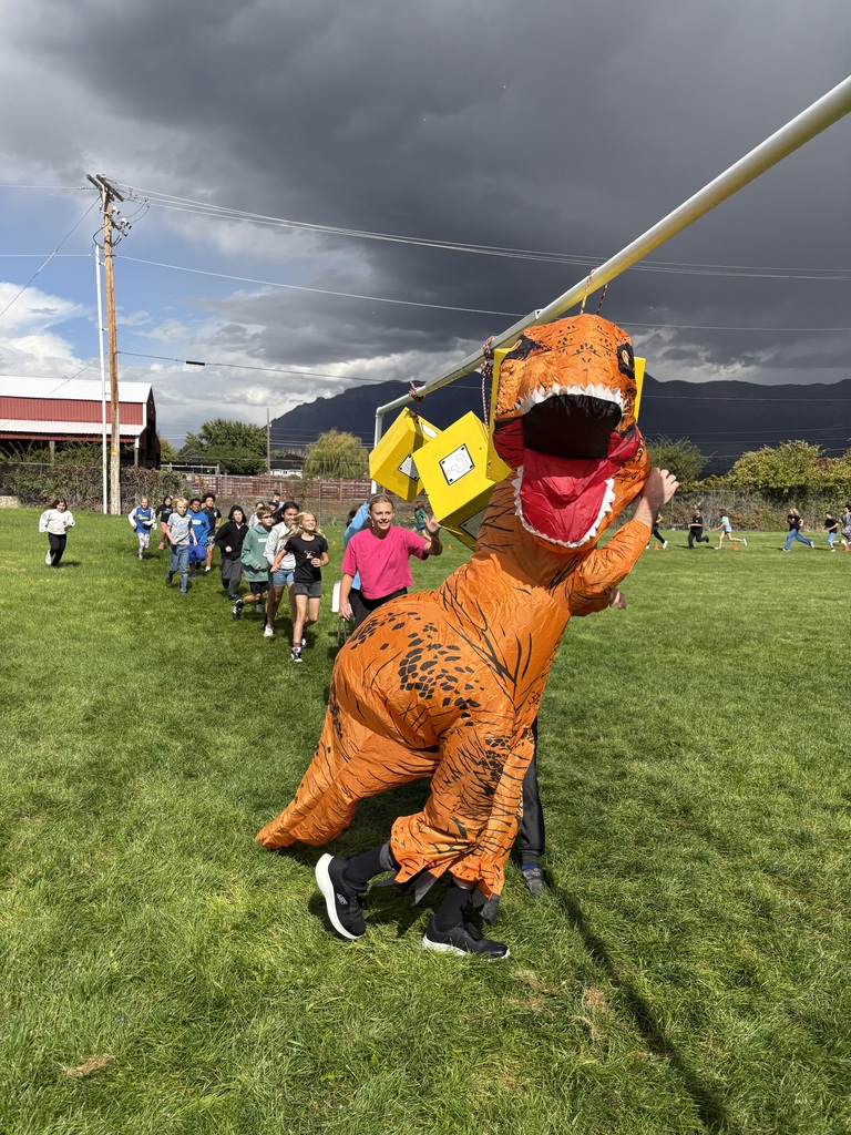 Teacher in blow up dinosaur costume running in fun run with students following