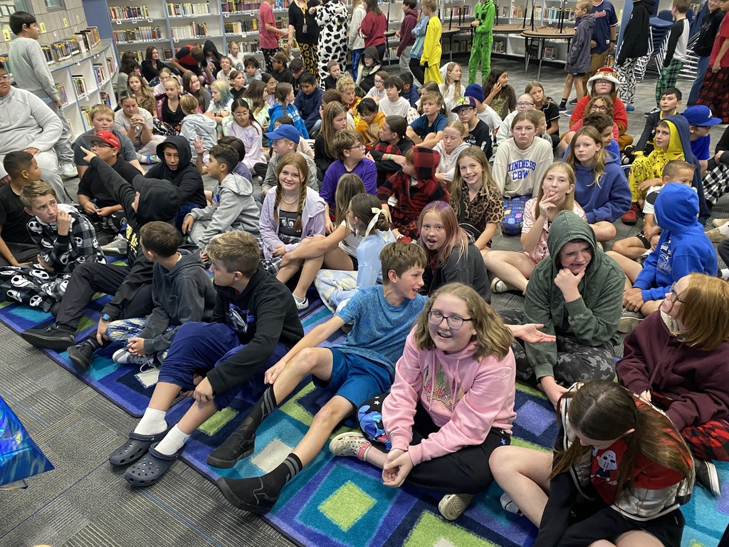 Students sitting and listening to a book read by a special visitor from the superintendents office.