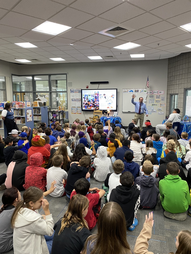Students sitting and listening to a book read by a special visitor from the superintendents office.