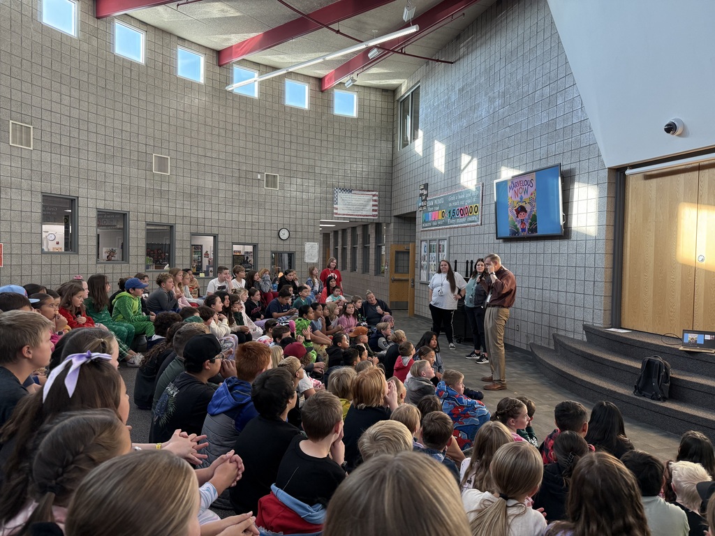 Students sitting and listening to a book read by a special visitor from the superintendents office.