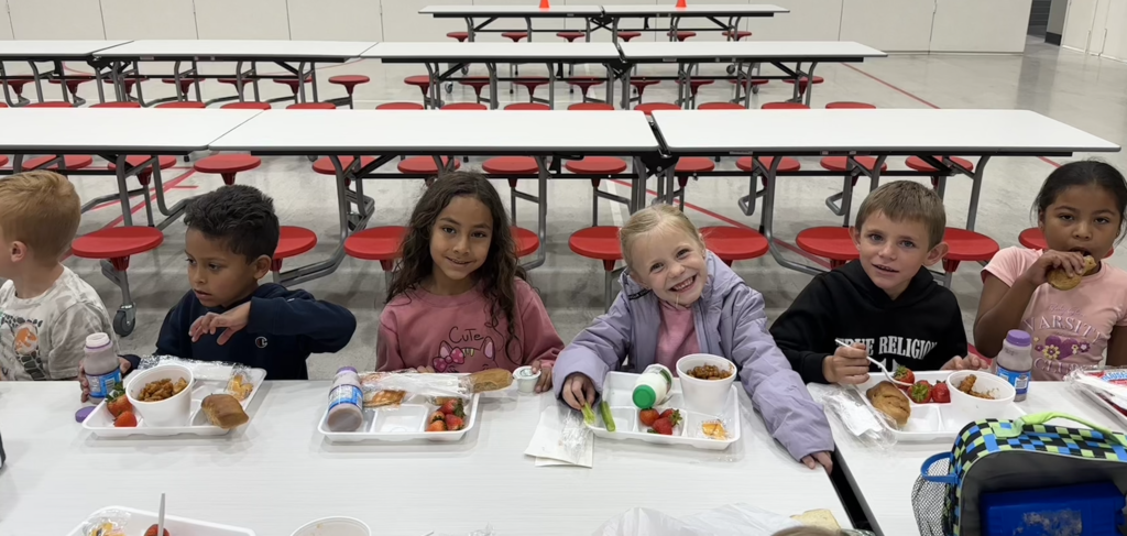 students sitting at lunch tables with smiling faces getting ready to  eat their  yummy school lunch