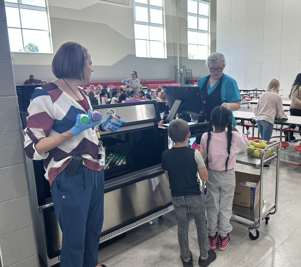 two adults helping students to get milk and scan their lunch cards