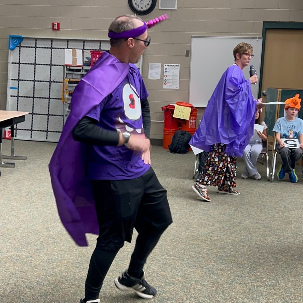 Sr. Findlay dressed as purple people eater and Mrs. Wayment singing