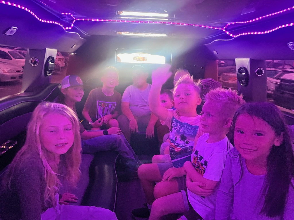 Farr West Elementary students posing excitedly by a limo for their prize ride, celebrating their excellent behavior and Blue Leader Bar achievement.