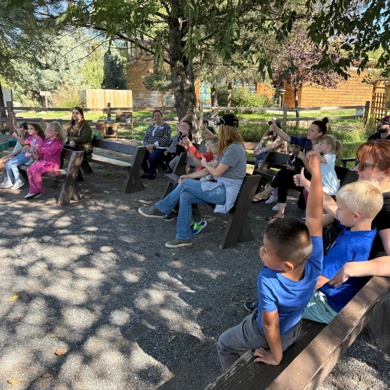students & chaperones sitting on benches listening to teacher