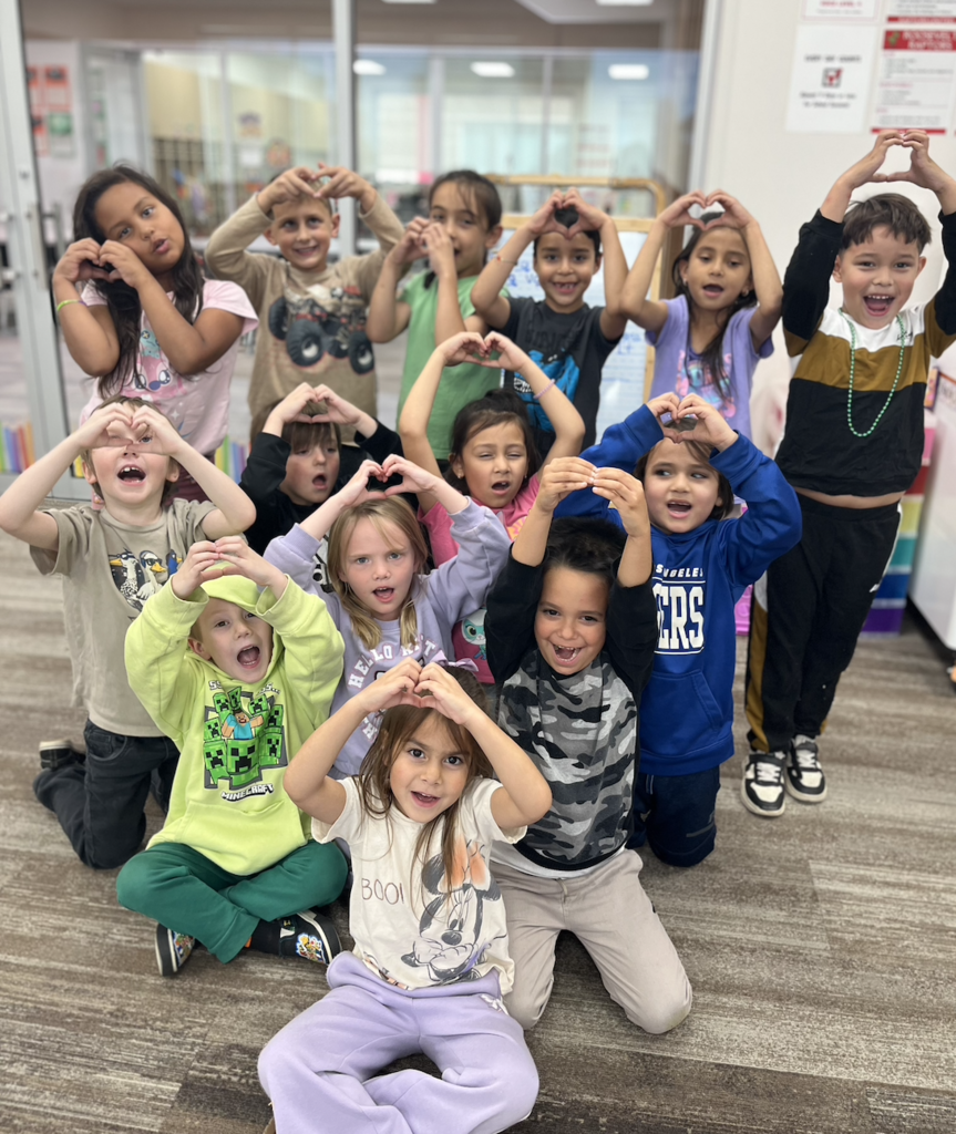 students sitting, kneeling, and standing in a pyramid shape. Students are making a hear shape with their hands.