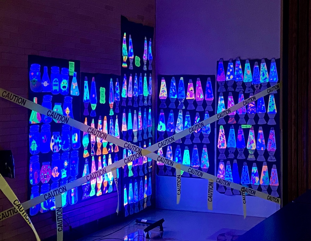 A dark room or hallway displaying a massive, glow-in-the-dark art project. Hundreds of cut-out paper shapes resembling lava lamps and jars are mounted on the wall and illuminated with blacklights, creating a vibrant, neon effect. Yellow caution tape is draped across the front.