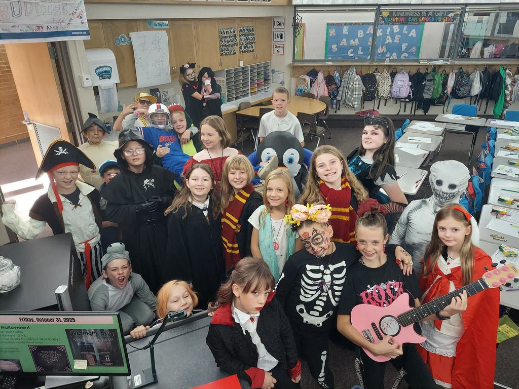 Several students in Halloween costumes (including a skeleton with painted face, a hooded figure, and a girl in a red dress) playing Twister on the classroom floor.
