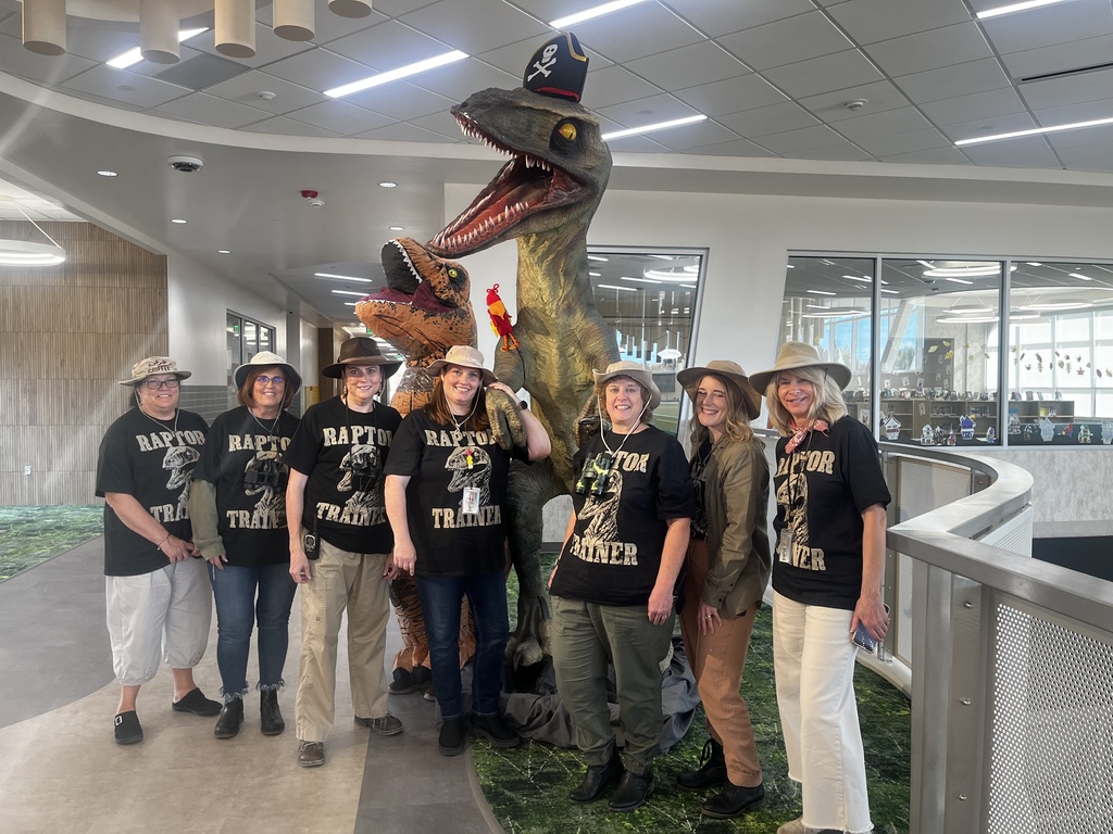 Office staff posing with a large raptor dinosaur. They are all dressed as raptor trainers