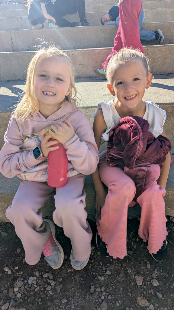 Two young girls sitting side-by-side on concrete steps, smiling happily for the camera.