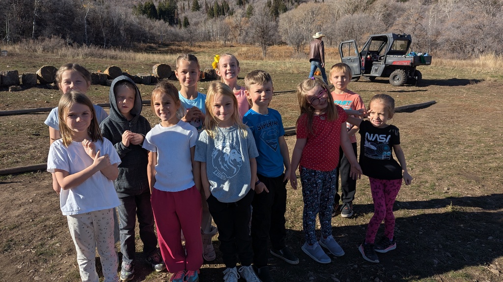 A group of ten 2nd grade students smiling and posing together for a photo in a grassy, open outdoor area.