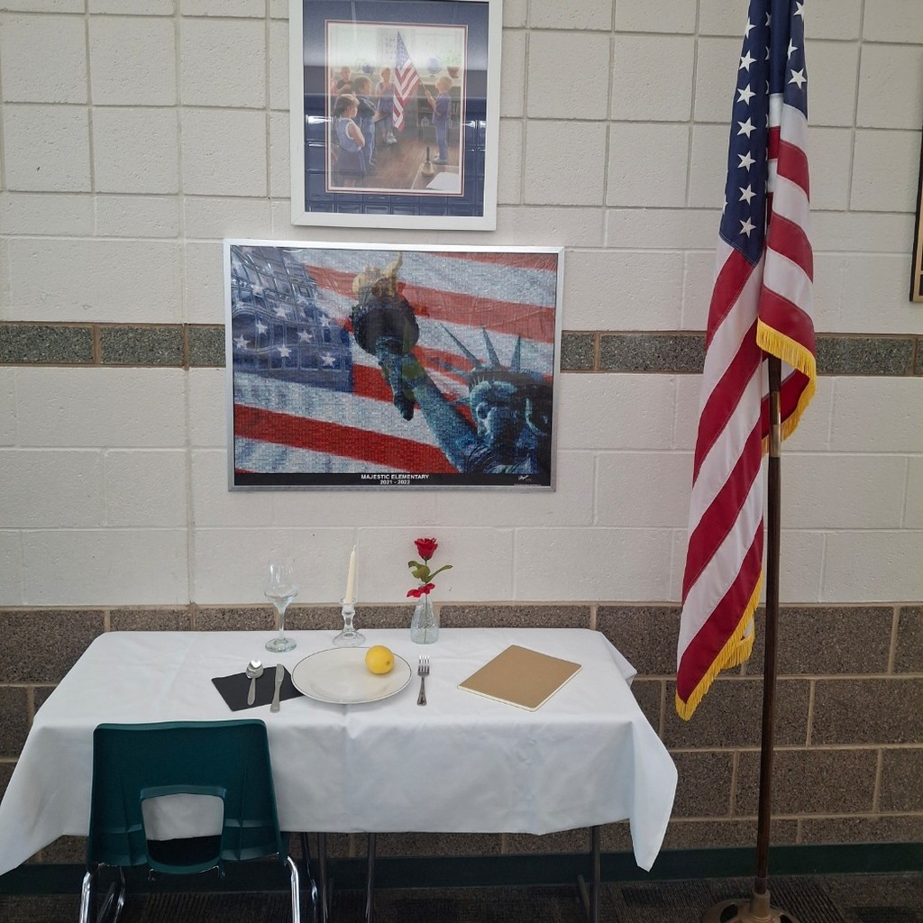 white table set with plate, lemon, salt black napkins, rose, and upside down goblet. next to an American flag