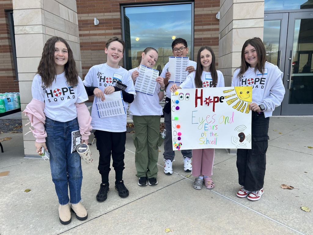 Students standing in front of a building holding up a poster that says "Hope, eyes and ears of the school"