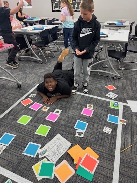 students making silly faces at the camera, playing a game with cards and pictures on the floor
