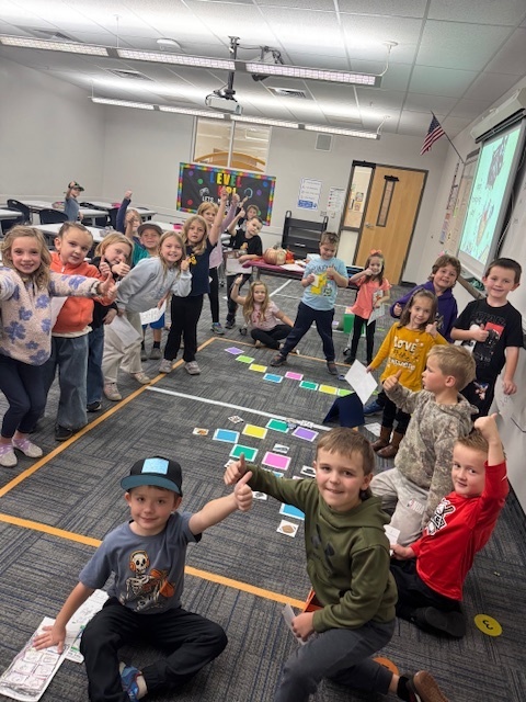 kids gathered around on the floor in the computer room, with thumbs up and smiles