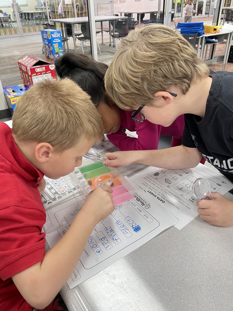 a group of three students working to examine different seeds with magnifying glasses