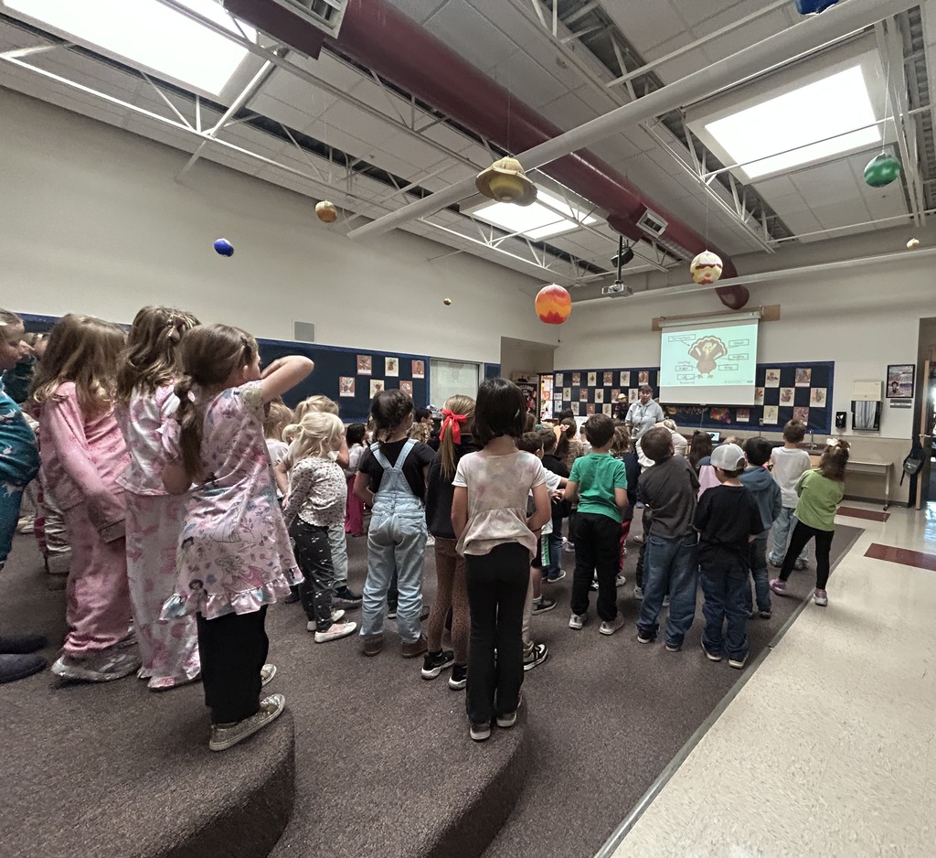 group of first grade students standing up and looking at a turkey and Mrs. Smith, they are singing
