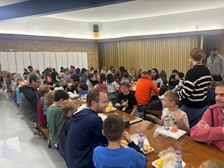 A photo of students in the lunchroom eating lunch with Rad Dads.