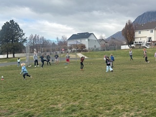 Kids playing kickball out at recess on the grass field with the Rad Dads.