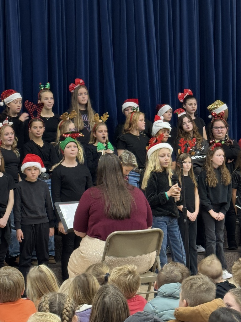 choir teacher sitting in a chair and students singing wearing christmas festive headbands