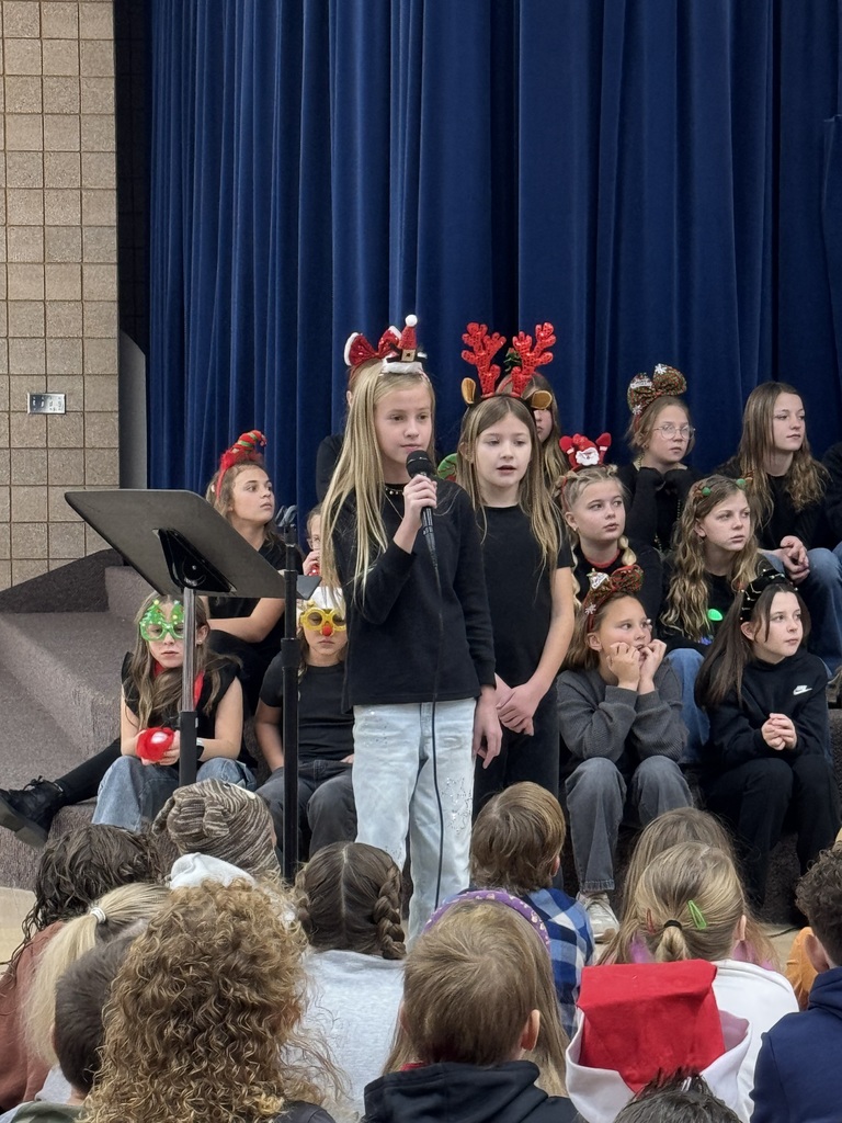two students singing in the microphone and students watching a choir sitting behind them