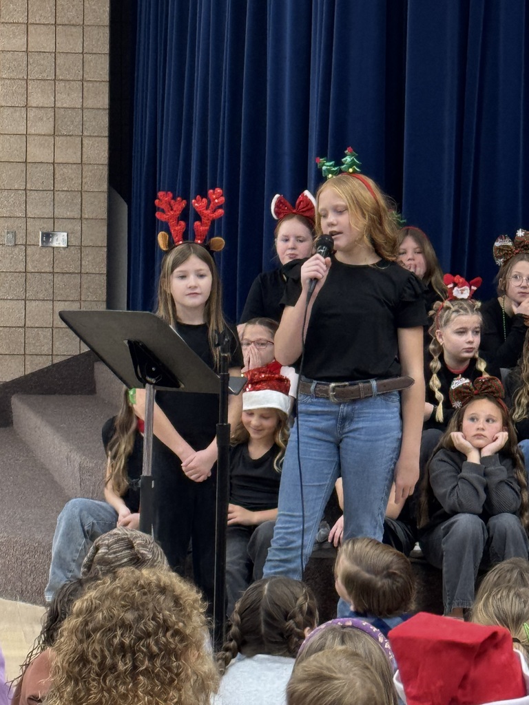 two students talking in a microphone with other choir students sitting behind them