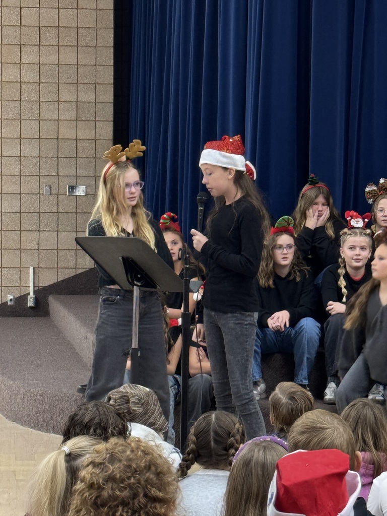 students talking in a microphone and choir students singing behind them