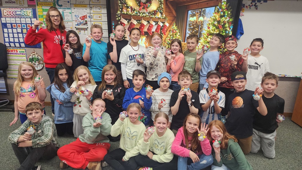 Students posing in front of camera holding ornaments they made