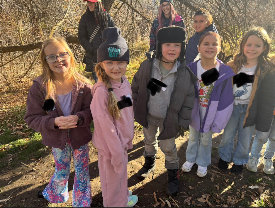 Five young girls smiling for a photo on a wooded trail. One girl wears a grey beanie with "HAVEN BAY" embroidered on it, and another wears a purple jacket over a white T-shirt featuring a Grinch graphic and the words "Merry Grinchmas."