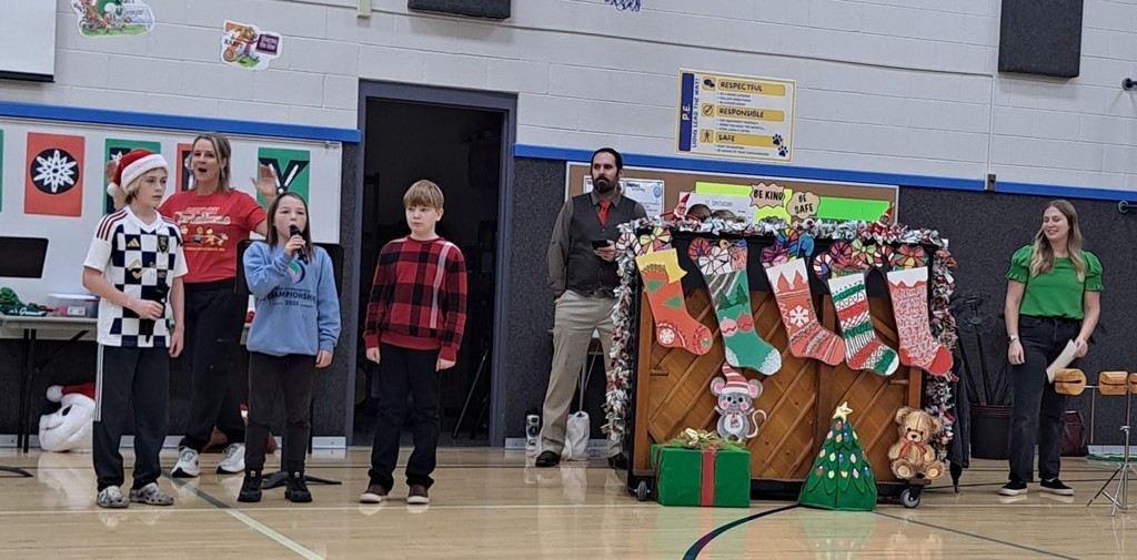 Three student soloists performing in front of a decorated piano with oversized holiday stockings.