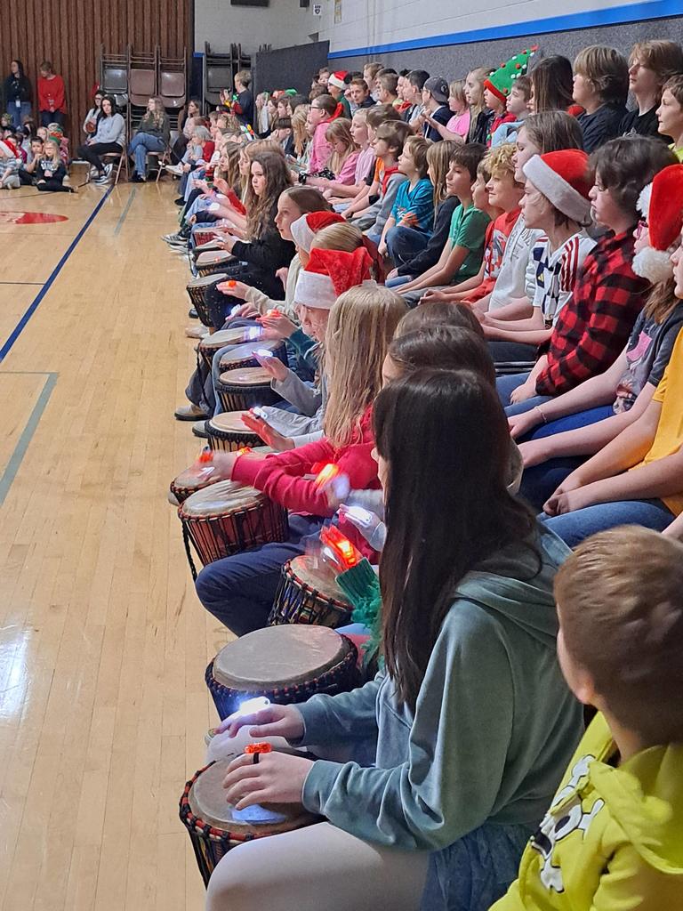 A close-up side view of students’ hands with glowing lights as they play a rhythm on their drums.