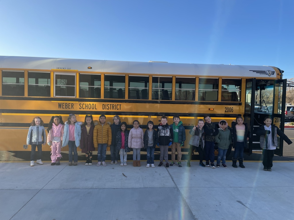 First grade class standing along the side of a school bus getting ready to go on their field trip
