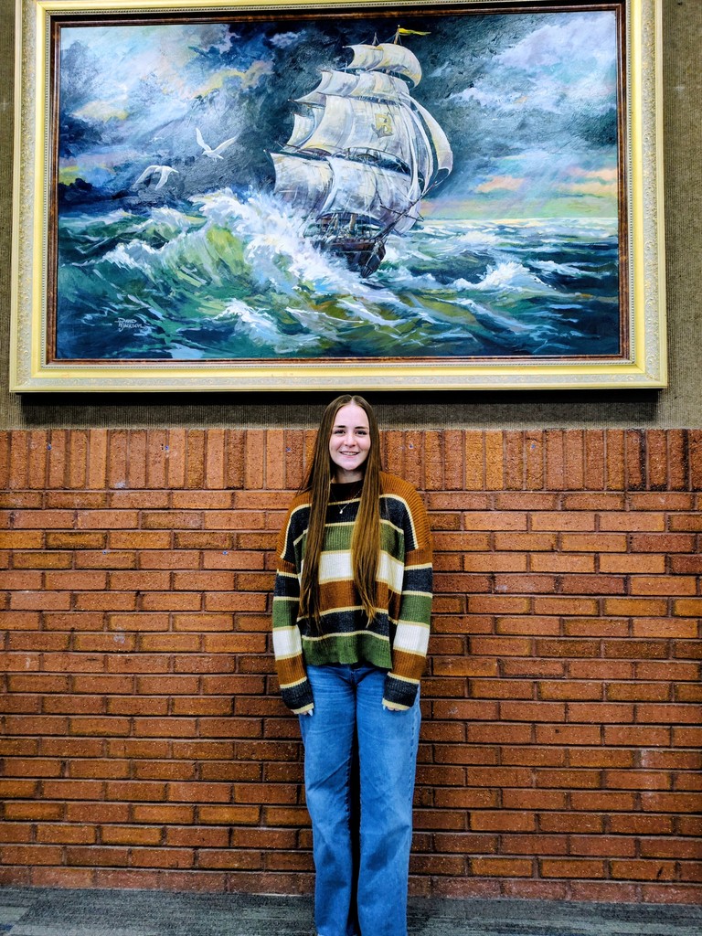 Laker Haylie Rice standing in front of a brick wall and painting.