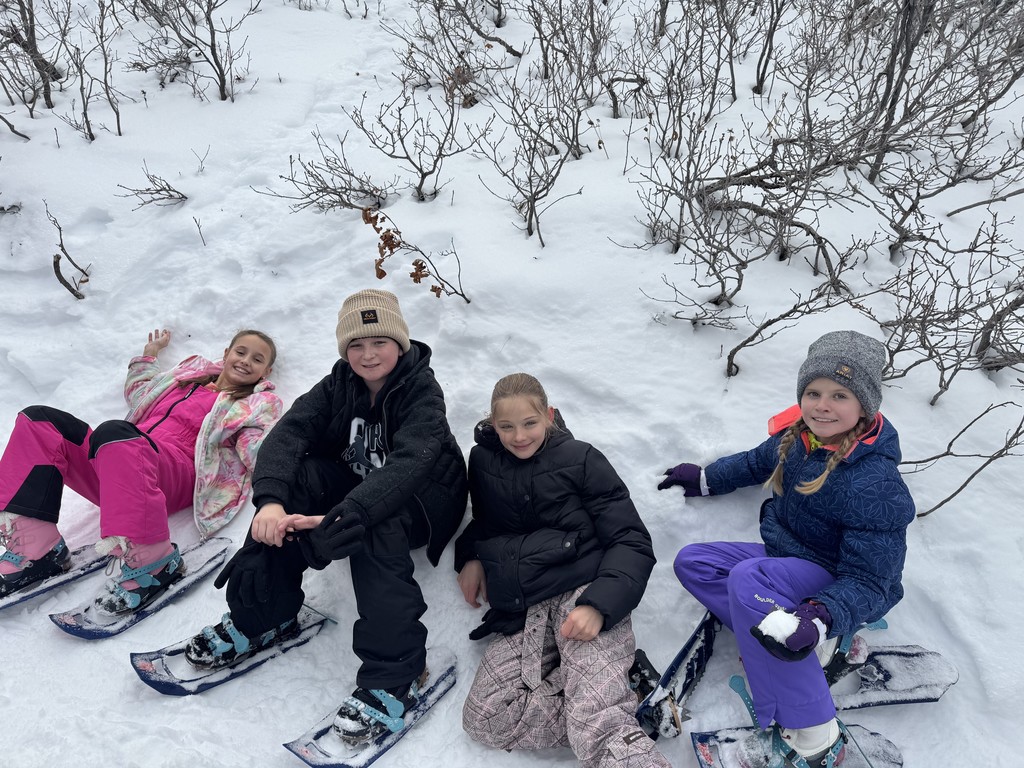 four kids laying in snow with snow shoes
